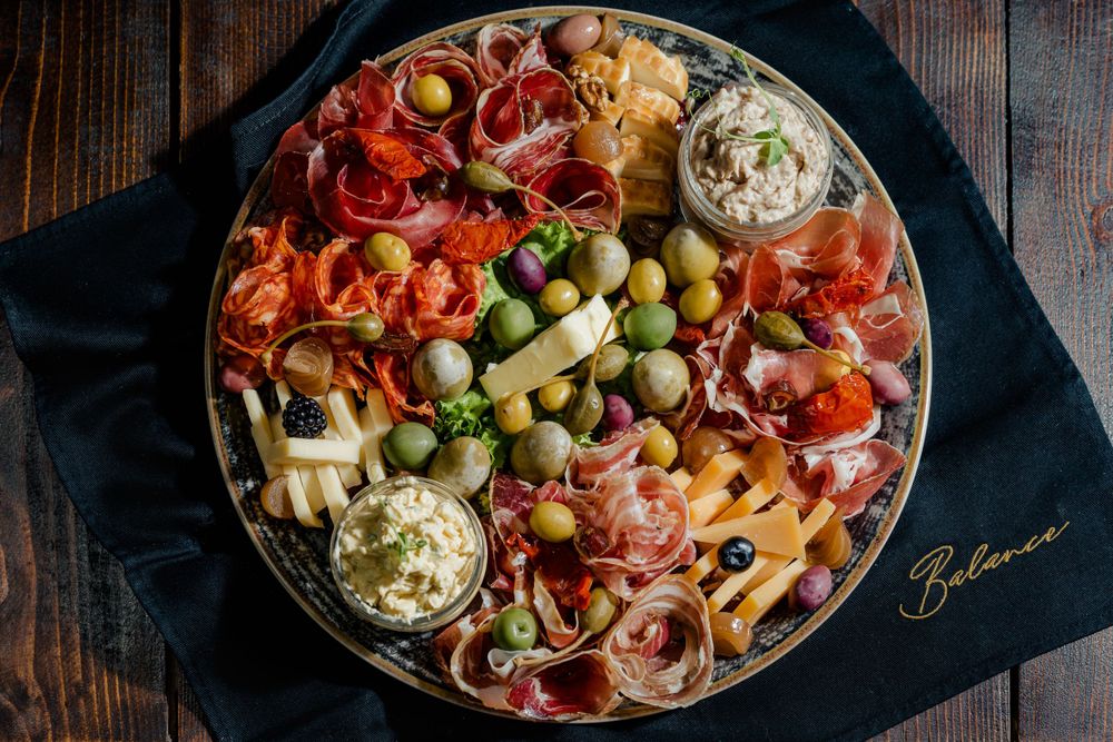 Charcuterie board with assorted meats, cheeses, olives and dips arranged on dark wooden surface.
