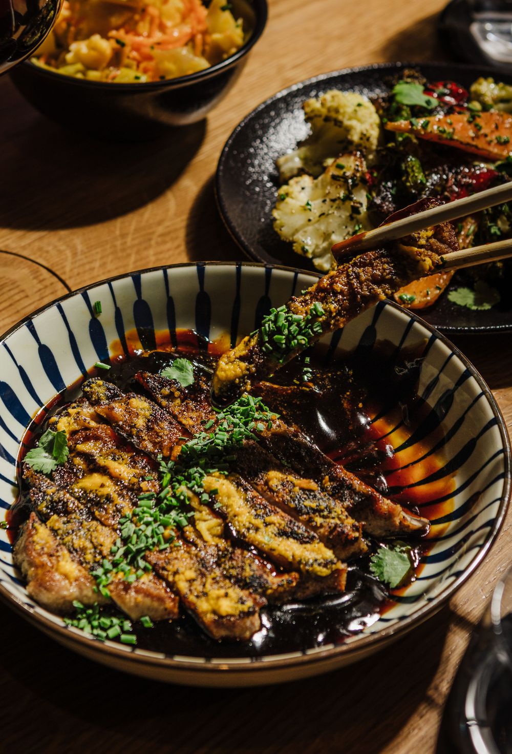 Grilled meat dishes garnished with fresh herbs served in traditional blue and white striped bowls.