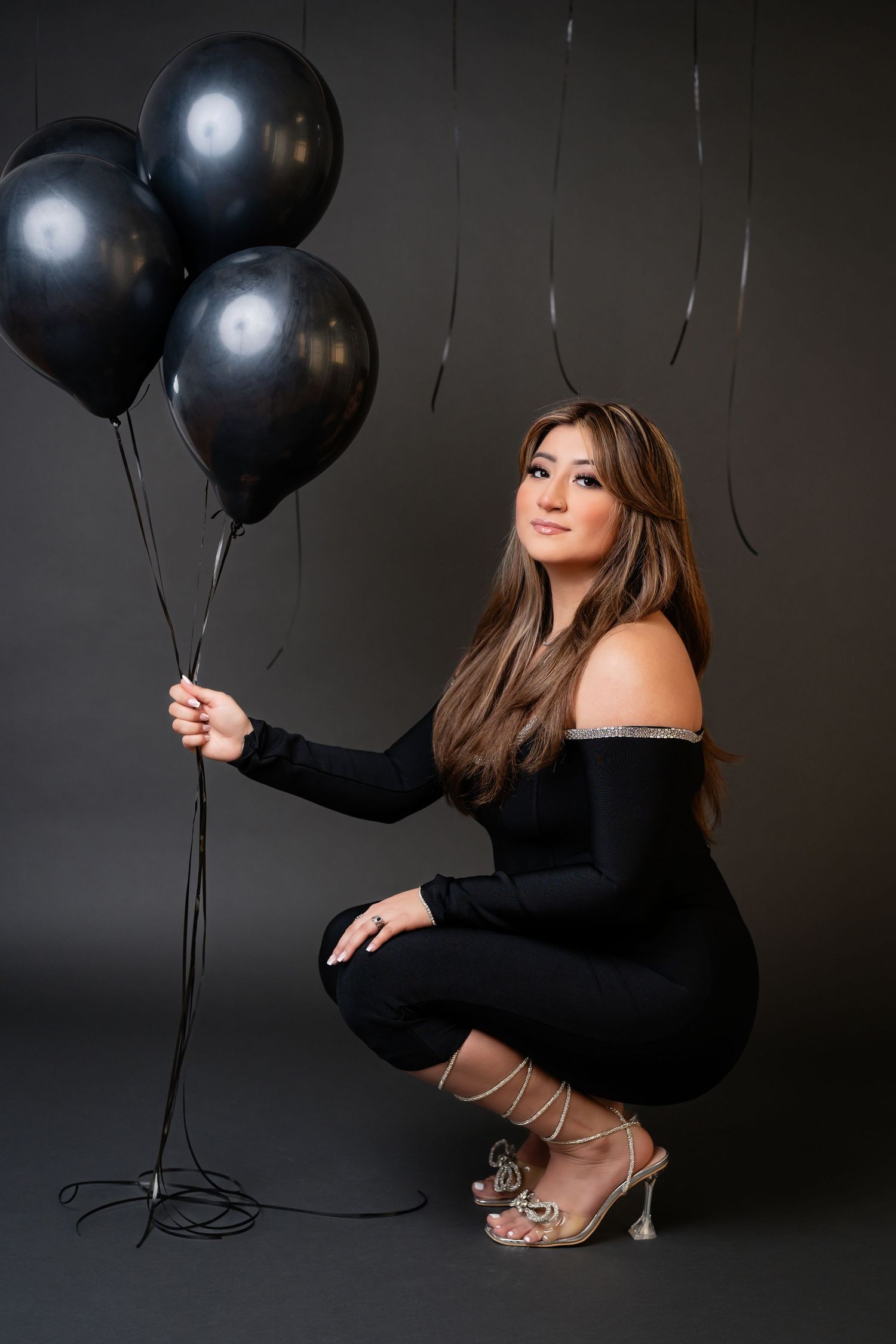 Moody portrait session with black balloons against dark background featuring glamorous styling.