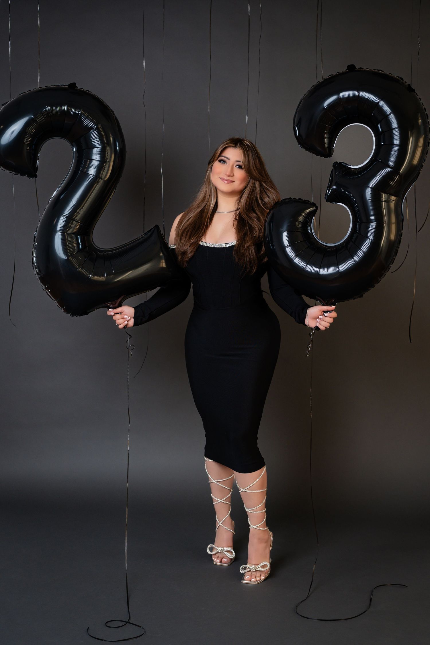 Stylish portrait session with large black number balloons in dark studio setting.