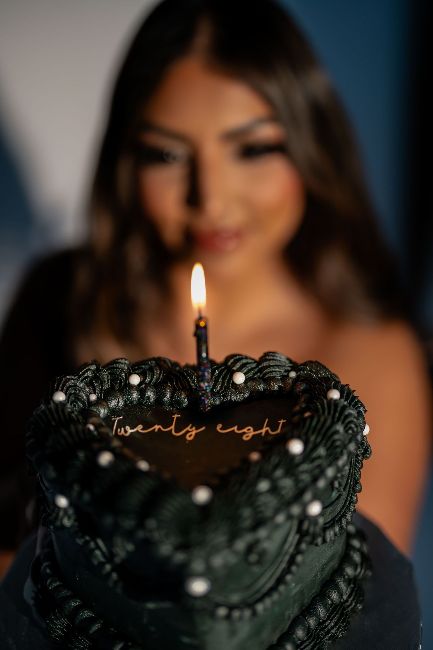 Dark birthday cake decorated with pearls and single lit candle.