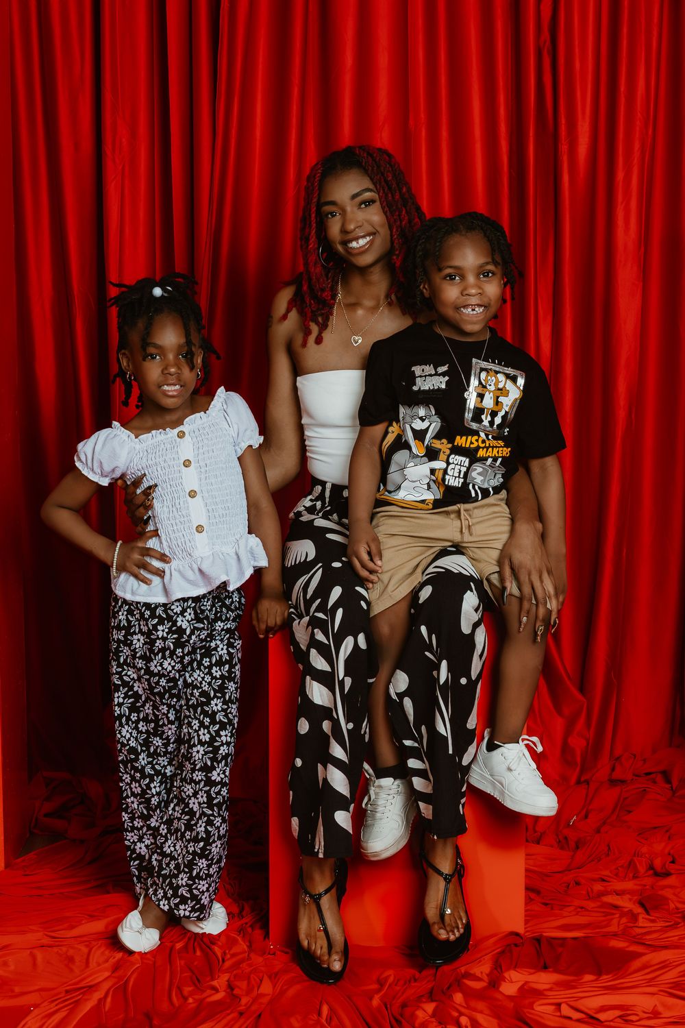 A woman and two children pose together in front of a red curtain backdrop in a studio portrait.
