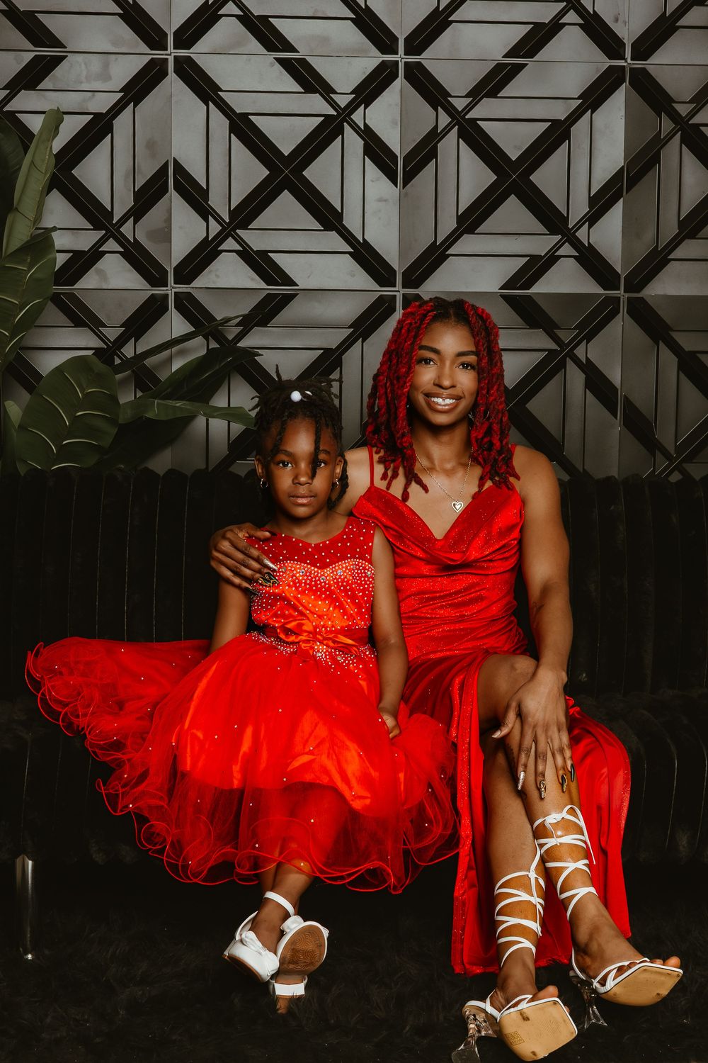A woman and young girl in matching red dresses pose together, smiling for a portrait photo.