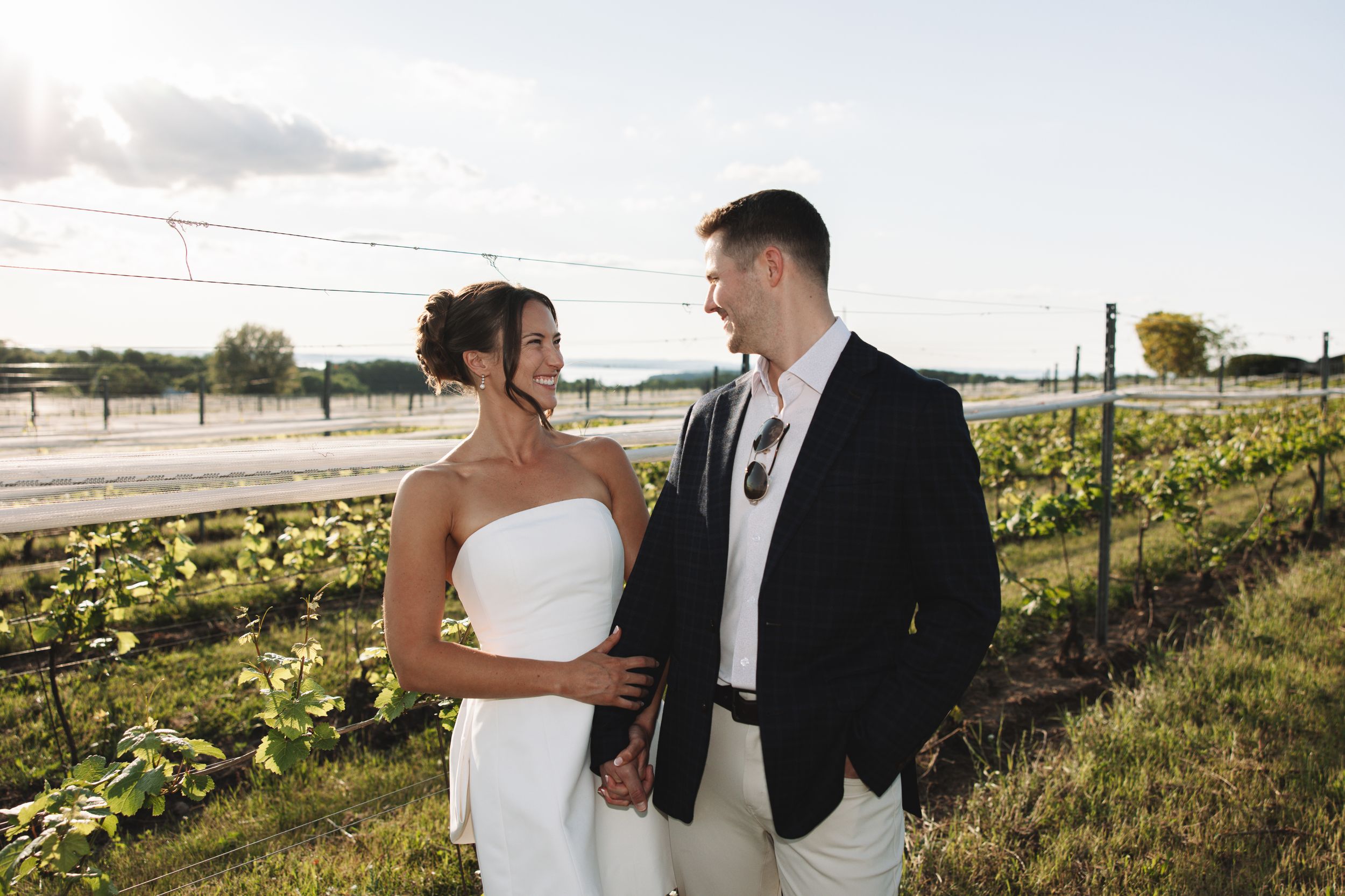 Bride and groom walking through a vineyard during a rehearsal dinner at a winery