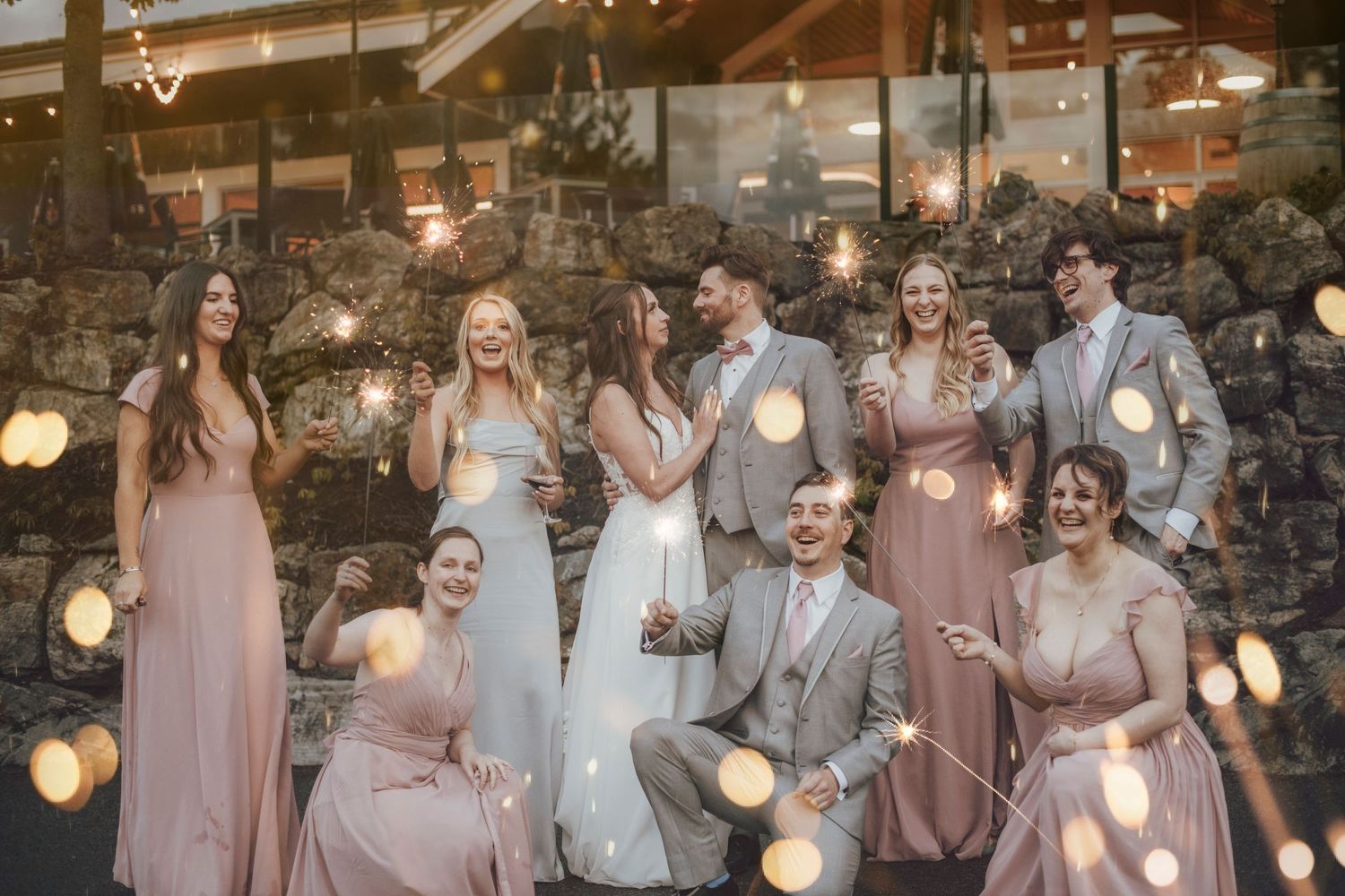 Wedding party gathered under string lights at outdoor celebration.