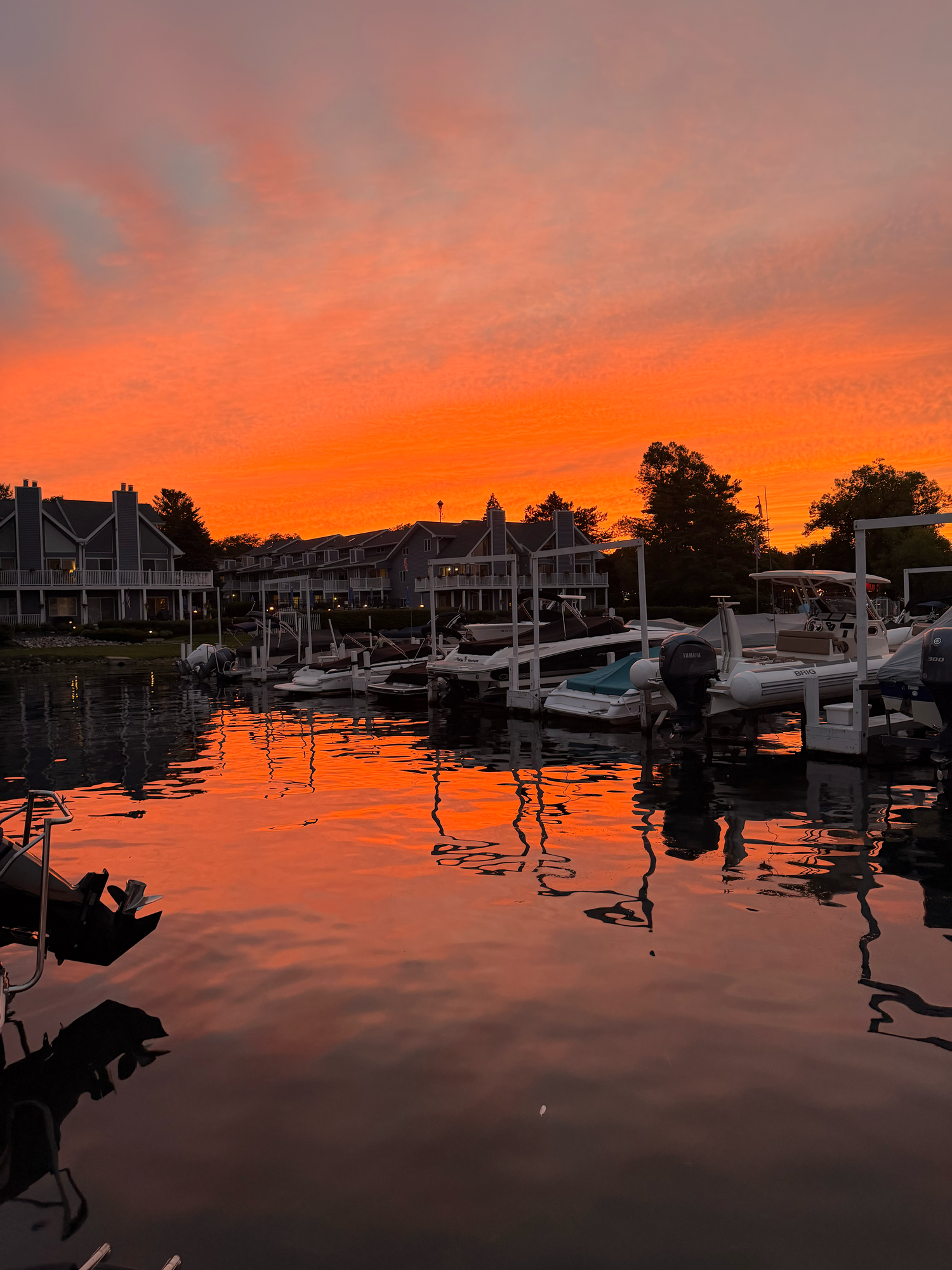 Stunning orange and red sunset reflecting over a calm marina with boats docked near waterfront homes.