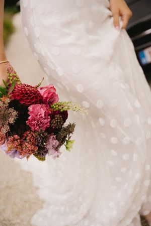 Close-up detail of a vibrant burgundy and pink bridal bouquet against a white wedding dress.