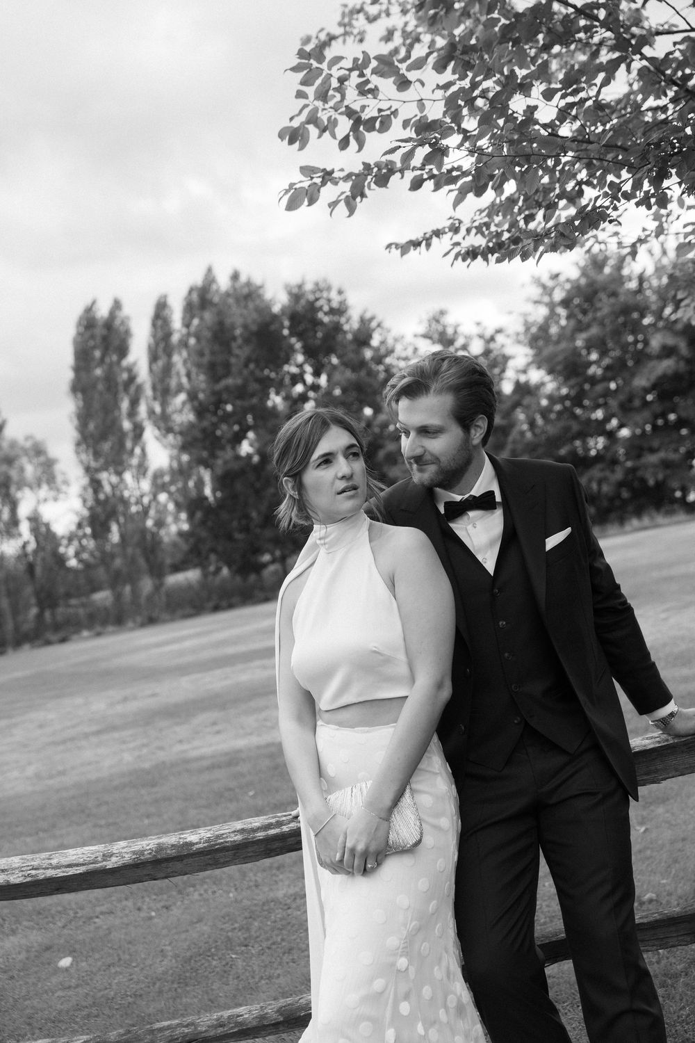 A black and white portrait of a couple in wedding attire standing in a grassy field.