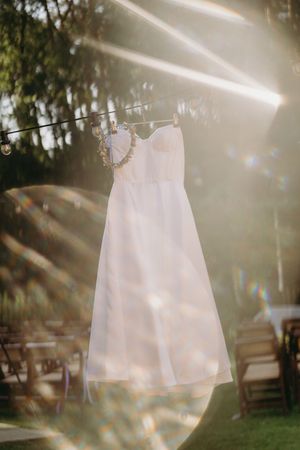 White dress hanging in sunlight creating an ethereal glow through trees.