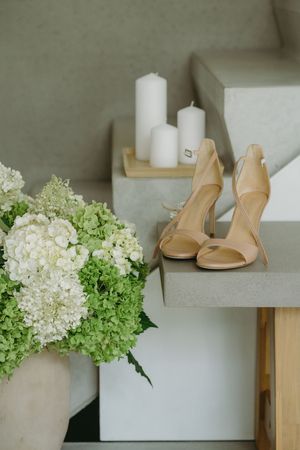 Wedding accessories including nude heels and white hydrangea flowers arranged on white shelves.