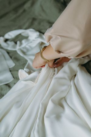 Detail shot of hands adjusting the pleats on an elegant white wedding dress.