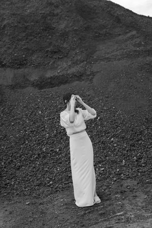 A figure in white dress walks along a dark rocky terrain.