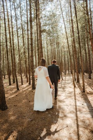 A couple walking through a sunlit pine forest with long shadows casting across the ground.