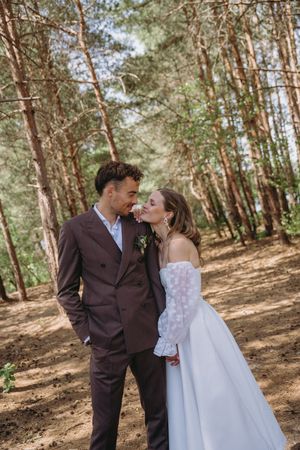 A couple shares romantic moments in a sunlit pine forest setting.