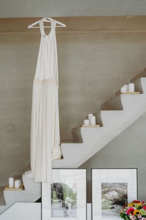White wedding dress hanging elegantly against a neutral wall with staircase and artwork.