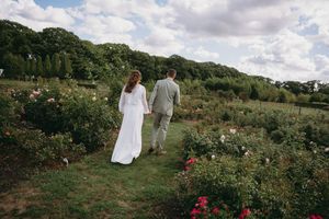 A panoramic view of a couple walking through a countryside garden on their wedding day.