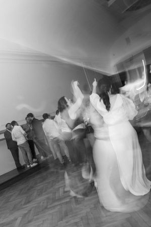Motion-blurred black and white photo of people dancing at an event.