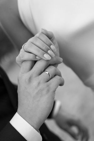 Black and white close-up of clasped hands showing wedding rings.