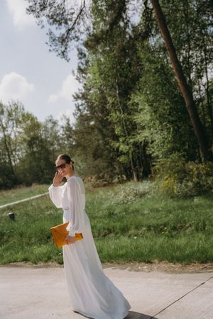 Person in flowing white dress walking through sunny outdoor setting.