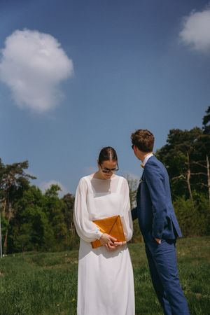 Wedding couple in white dress and navy suit posing in sunny outdoor setting.
