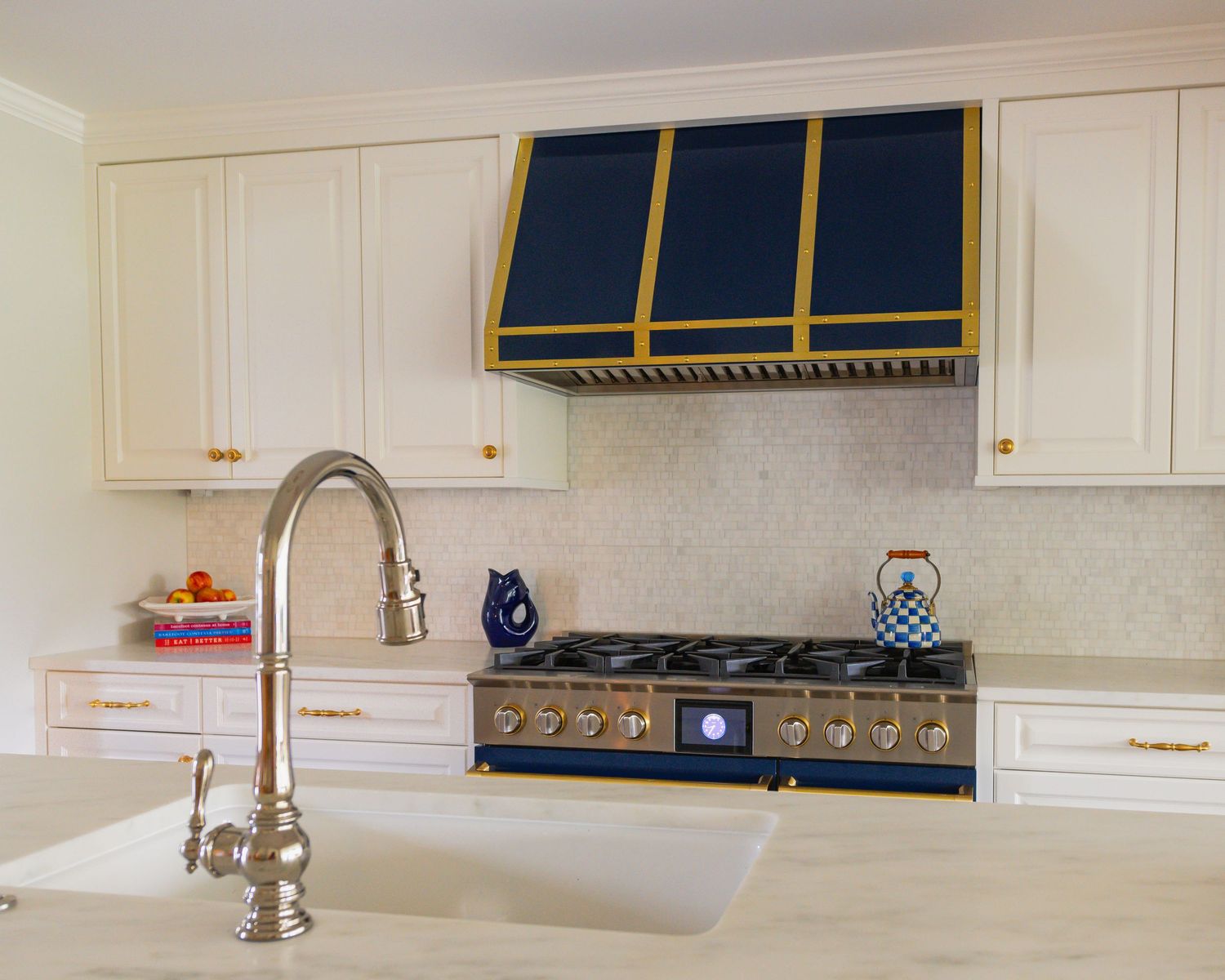 White kitchen with navy blue range hood, stainless steel appliances, quartz countertops and modern brushed nickel faucet.