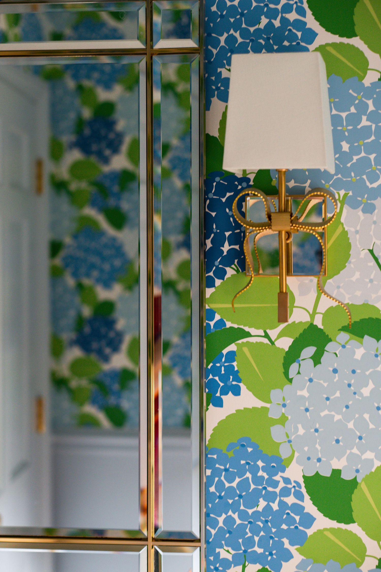 Gold wall sconce lamp against blue and green floral wallpaper creates elegant contrast in interior design.