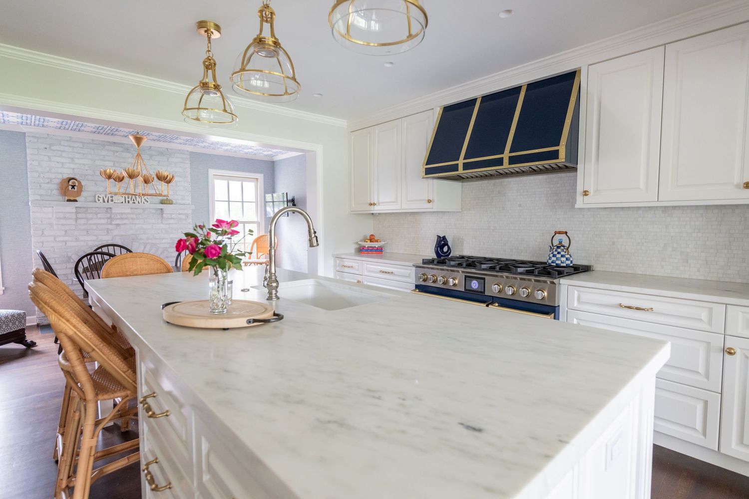 Elegant white kitchen with marble countertops, vintage pendant lights, and brass accents features a large central island.