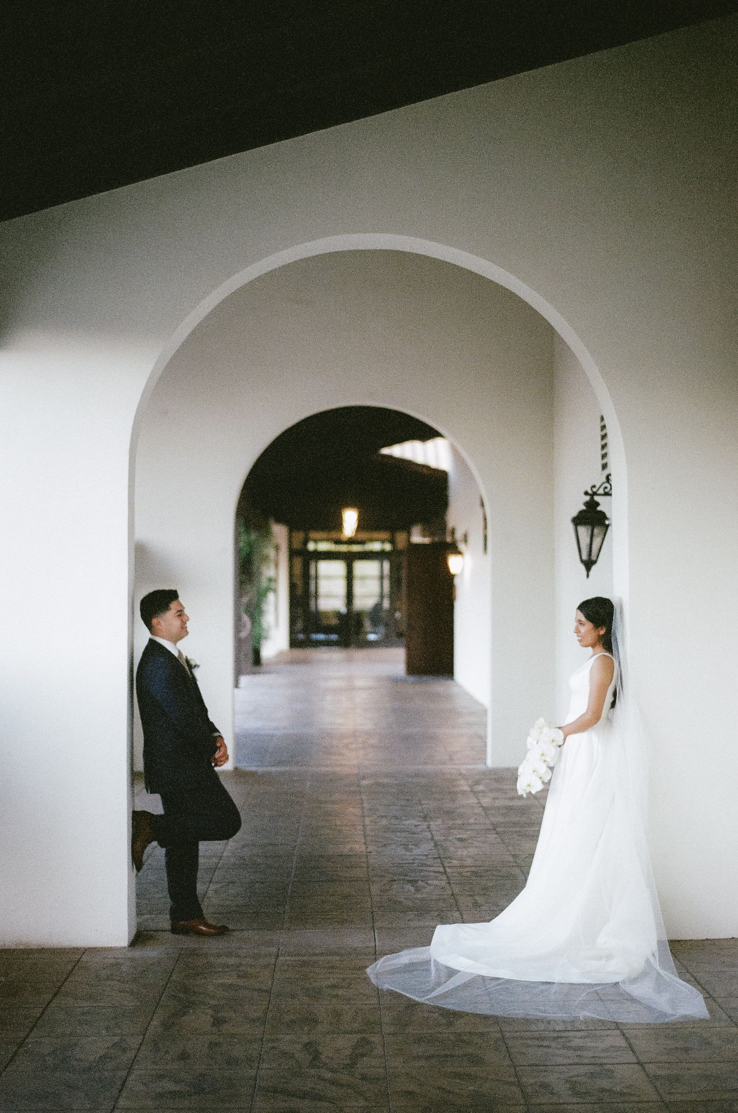Elegant wedding couple poses in an arched hallway with dramatic lighting.