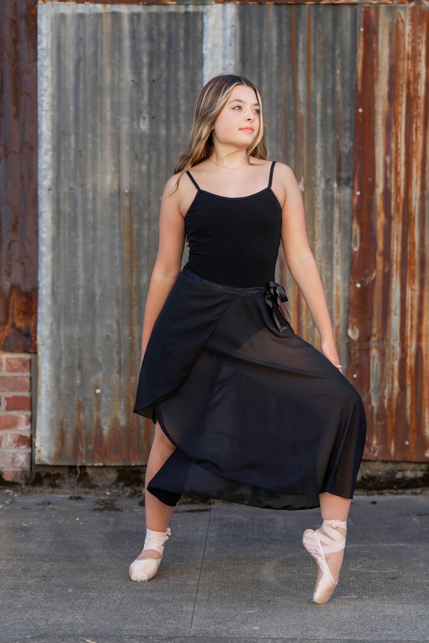 Ballet dancer en pointe in a black leotard and skirt against an urban metal backdrop – artistic dance photography in Portland, Oregon.