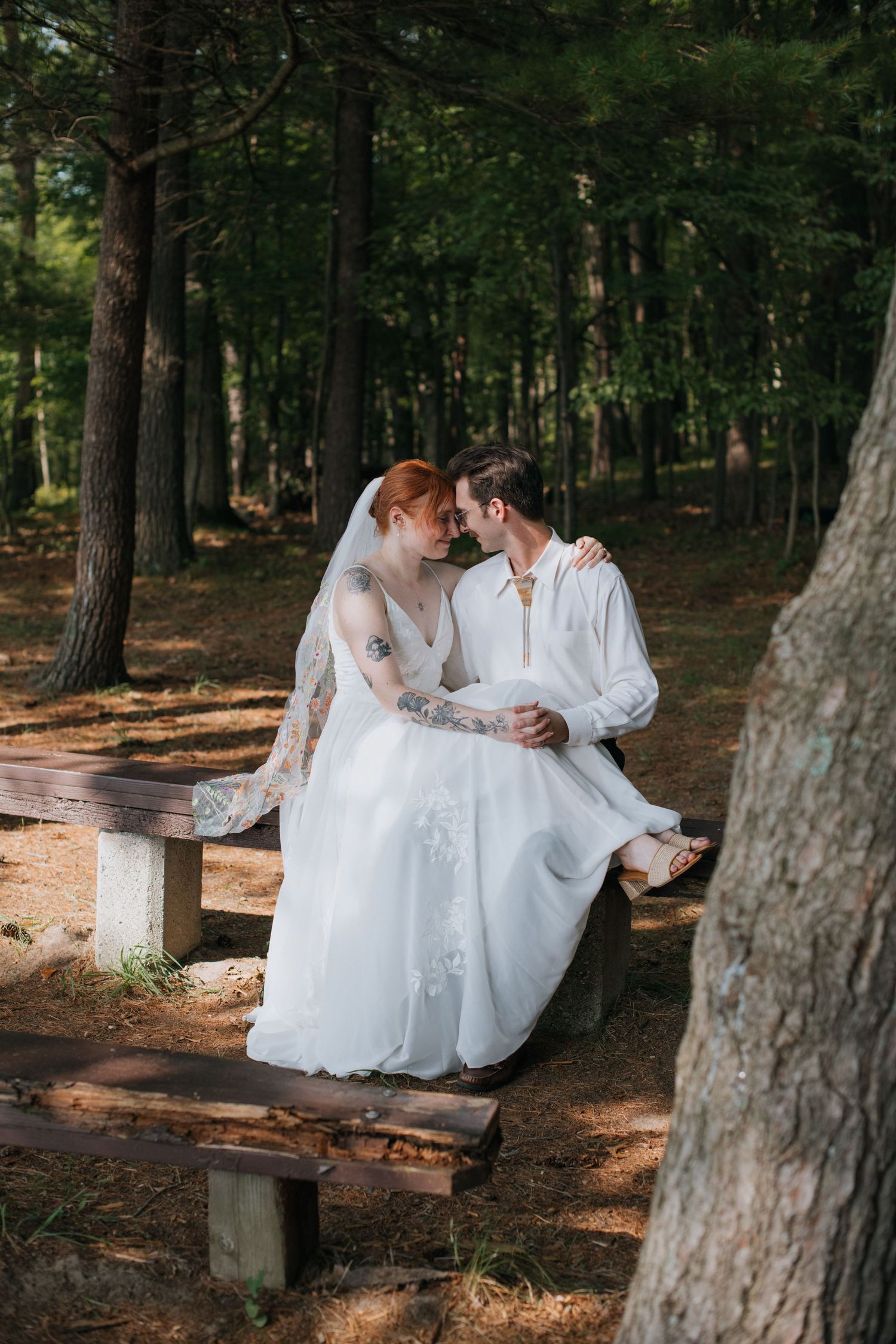 Intimate wedding portrait of couple sitting on wooden bench in serene forest setting.