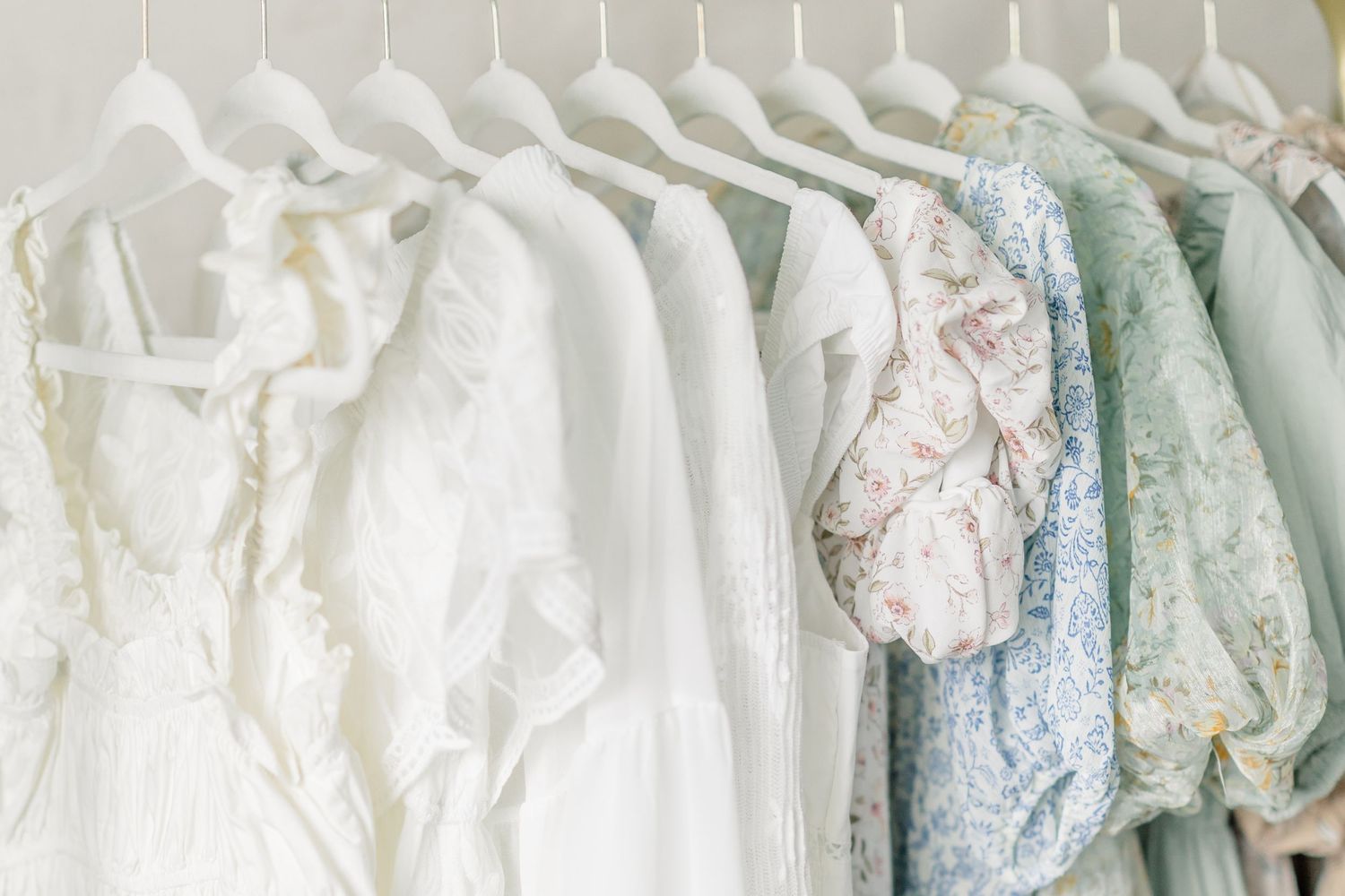 A row of white and pastel colored wedding dresses hanging on display in a bridal boutique.