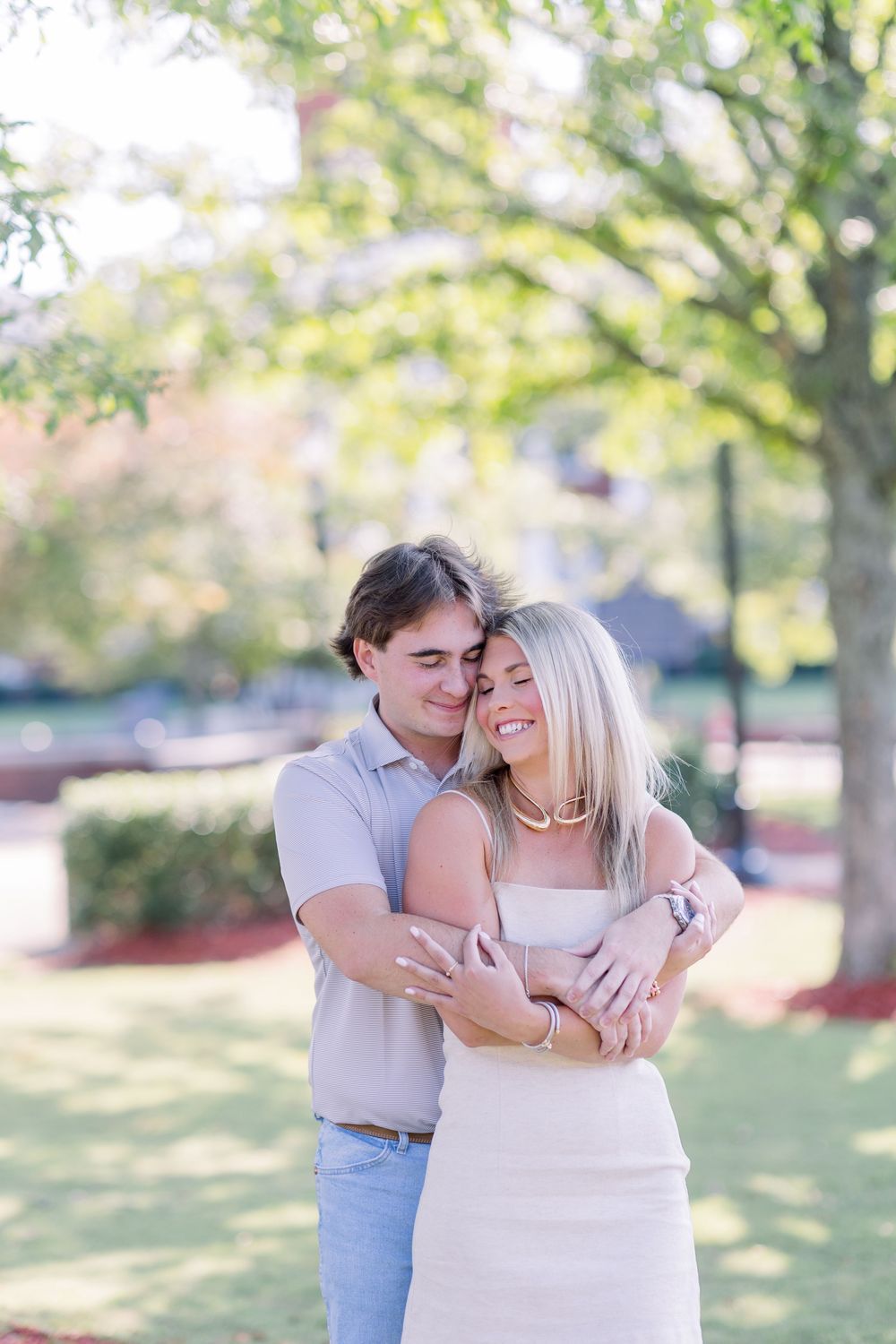 A couple embraces in a sunny outdoor park setting during a romantic photoshoot.