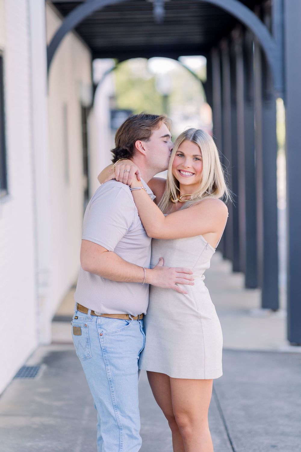 A couple embraces and shares a romantic moment under a covered walkway with white columns.