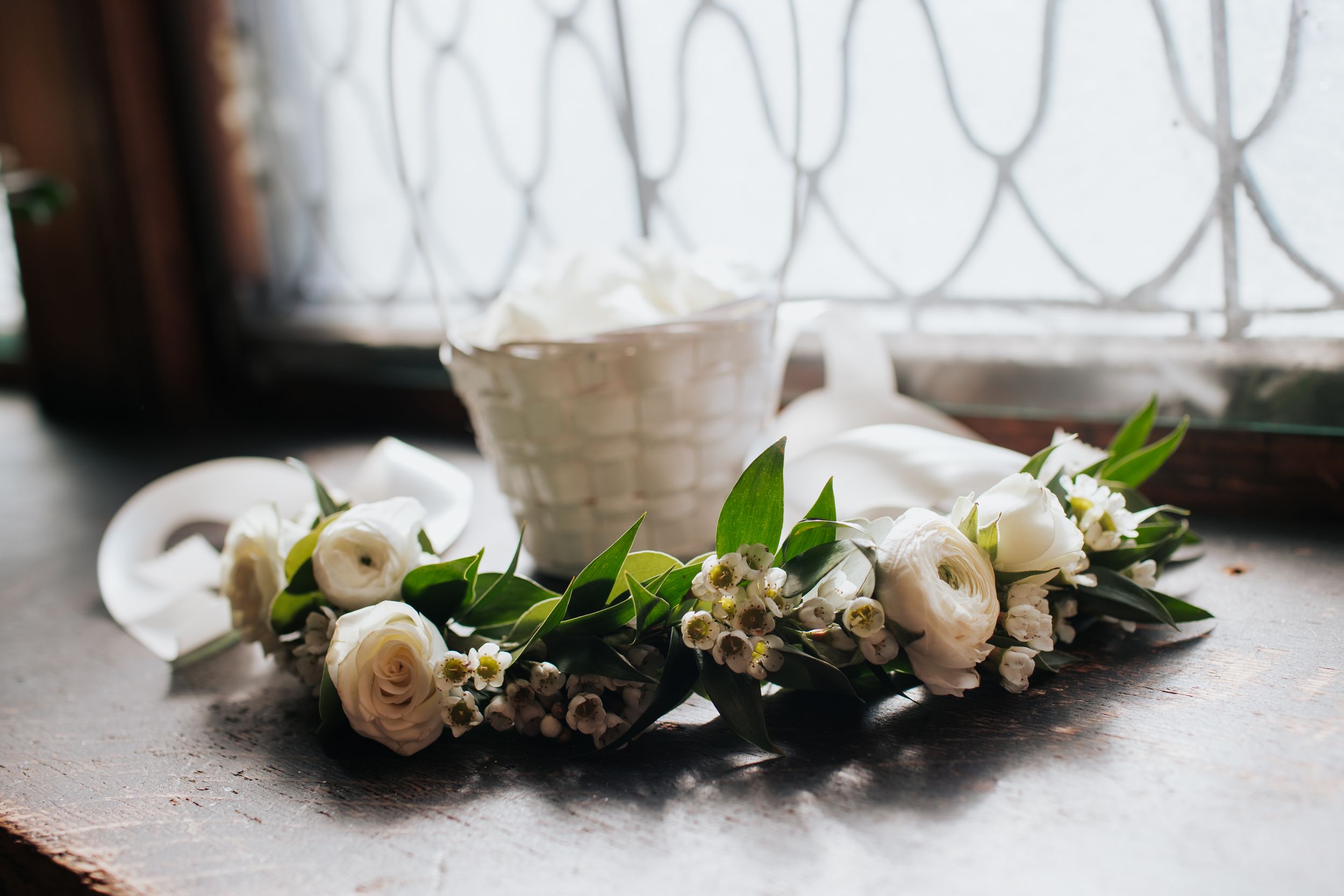 Delicate white roses and greenery arranged in a romantic wedding decor setting near an ornate window.