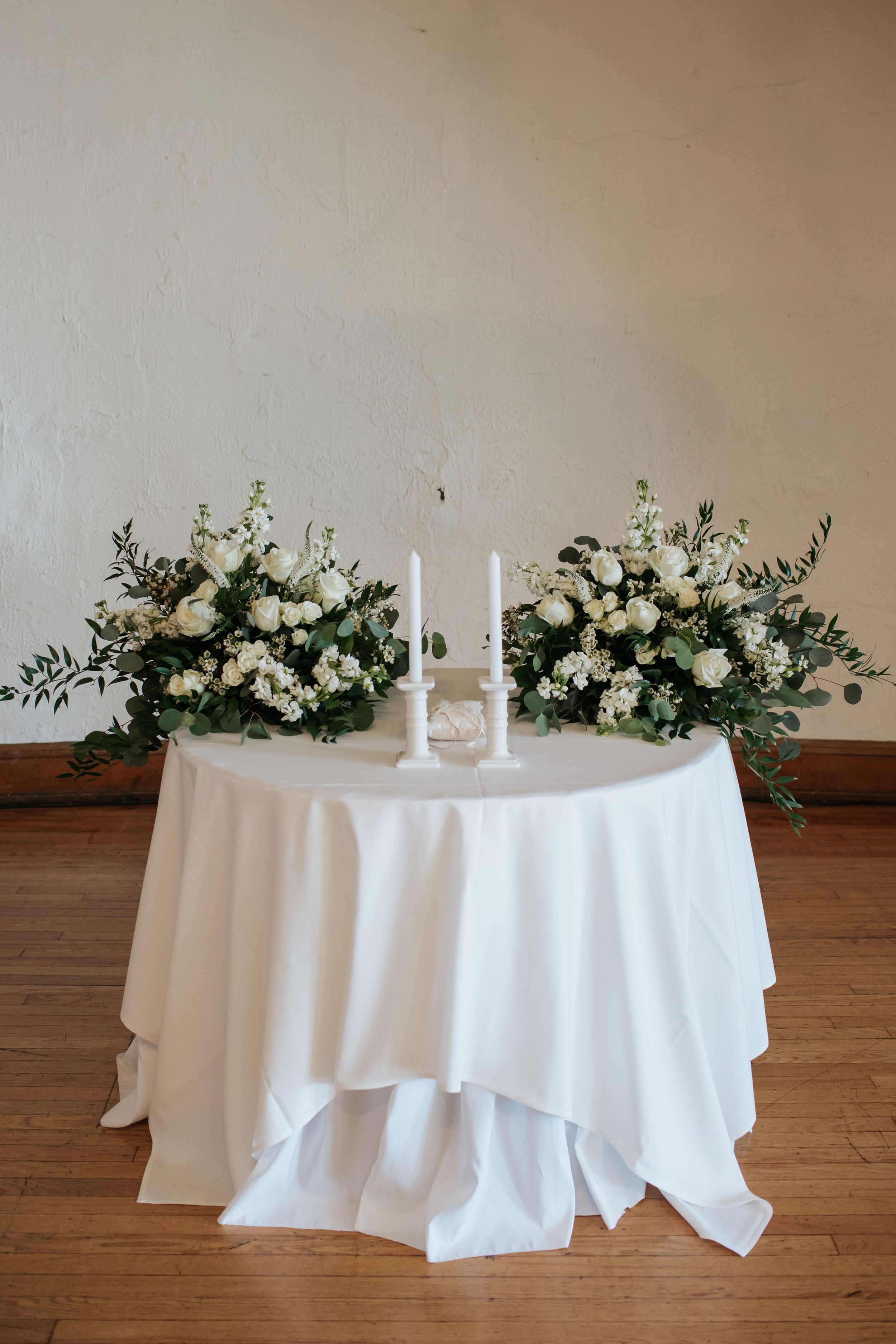 A white tablecloth covered round table decorated with elegant white floral arrangements and candles for an event.