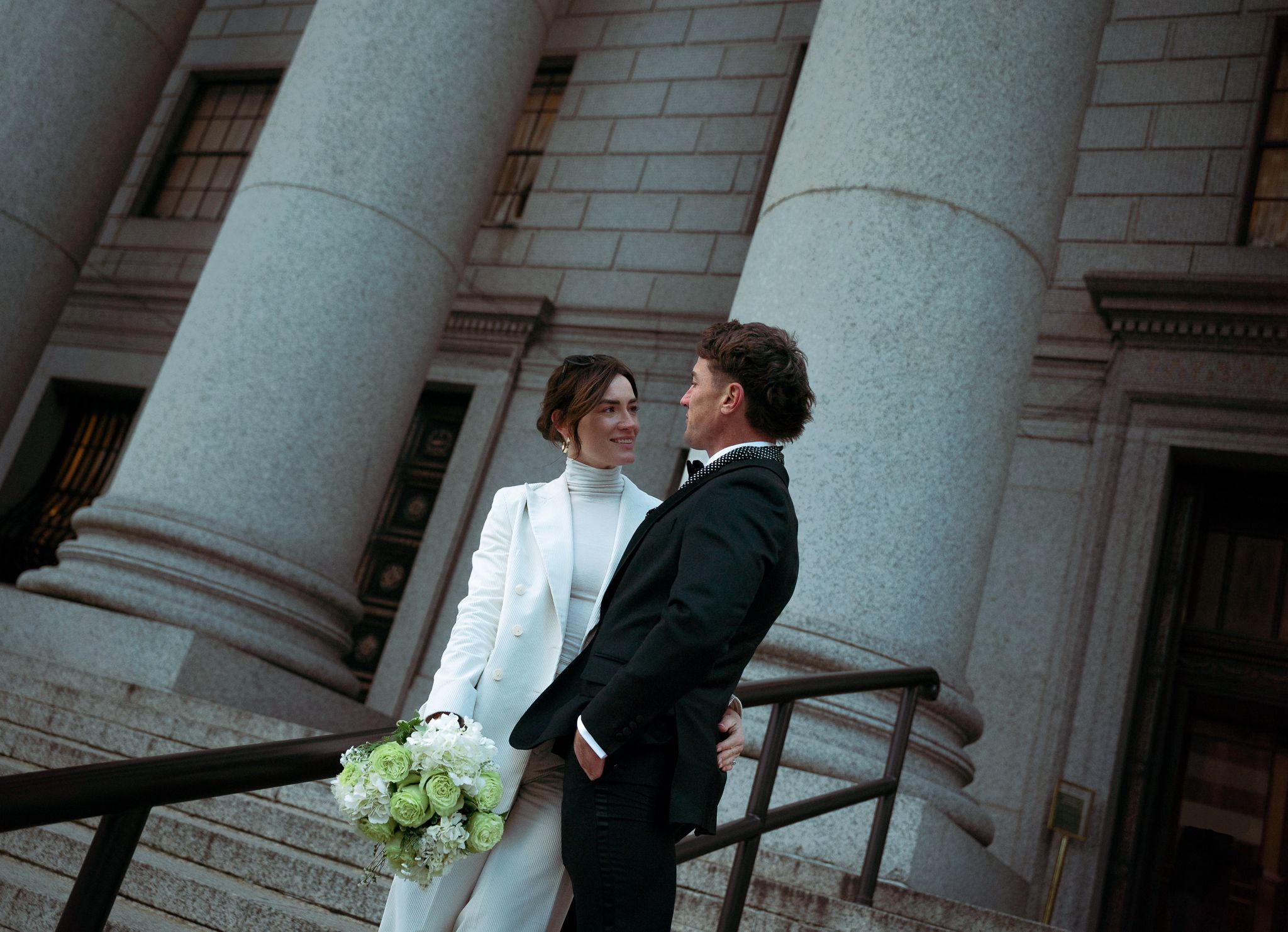 A couple shares an intimate moment between elegant stone columns of a historic building.