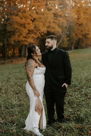 Newlyweds pose playfully in a field with autumn foliage creating a warm orange backdrop.