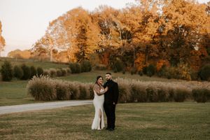 Wedding couple poses on a path with golden autumn trees and grass in the background.