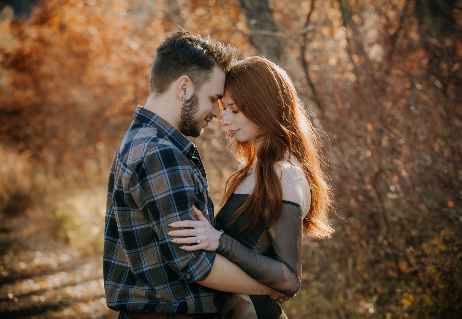 A romantic couple embraces in an intimate moment against a backdrop of warm autumn foliage.