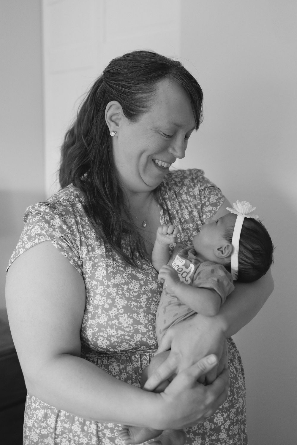 A woman in a floral dress shares tender moments with a newborn baby in a black and white photo.