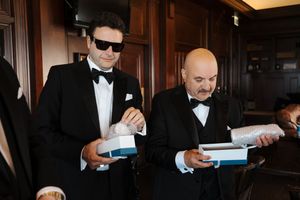 Four people in formal attire sign documents at a dark wooden table in an elegant room.