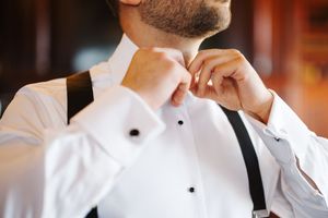 A person in a white chef's coat and black suspenders stands in a restaurant kitchen setting.