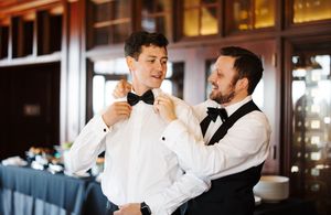 A groom and groomsmen in formal black tuxedos and white shirts prepare for a wedding celebration.