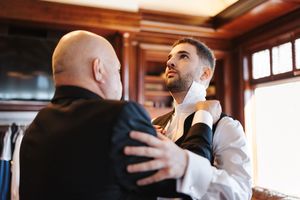 Wedding party members share emotional embraces and congratulations in a warmly lit indoor venue.