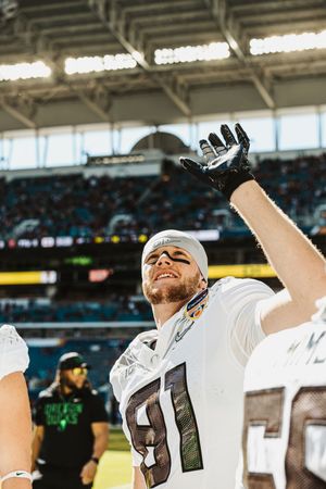 Football players celebrating with raised arms in white uniforms at Hard Rock Stadium.