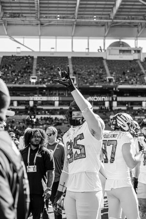Football players celebrate with raised arms in white uniforms on the field after a victory.