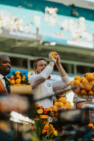 Vendors displaying and juggling fresh oranges at a stadium concession stand with bright citrus fruits on display.