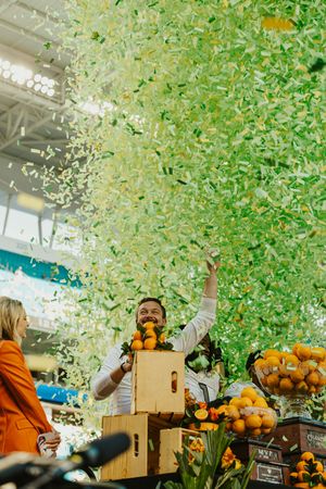 Green and gold confetti rains down over boxes of oranges at a celebration event.