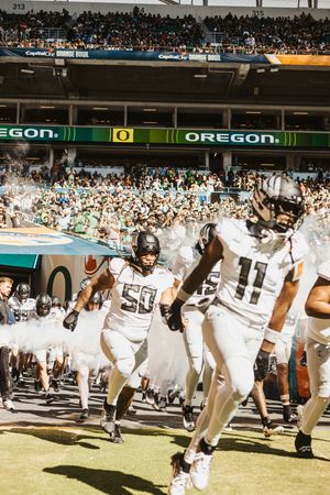 Oregon football team players in white uniforms perform synchronized movements on the field.