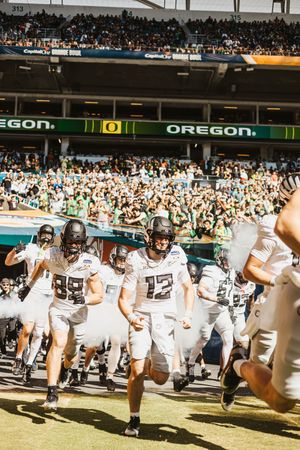 Football players in white uniforms running onto a field in front of a crowded stadium during a game entrance.